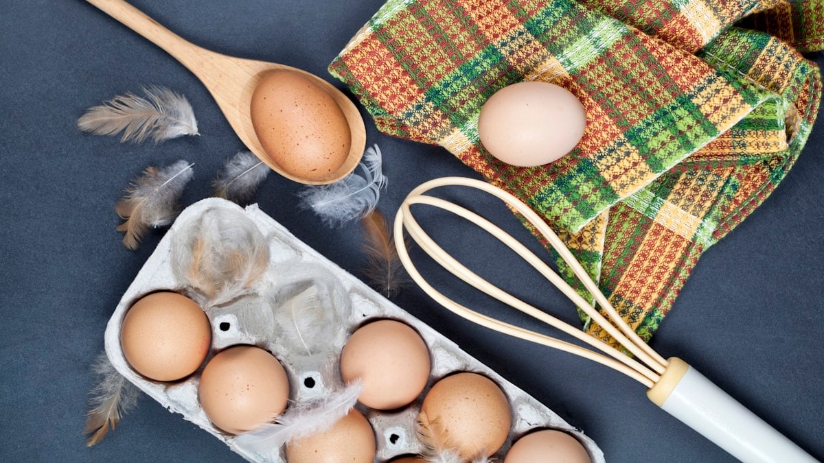 A bunch of eggs sitting in a carton next to a whisk